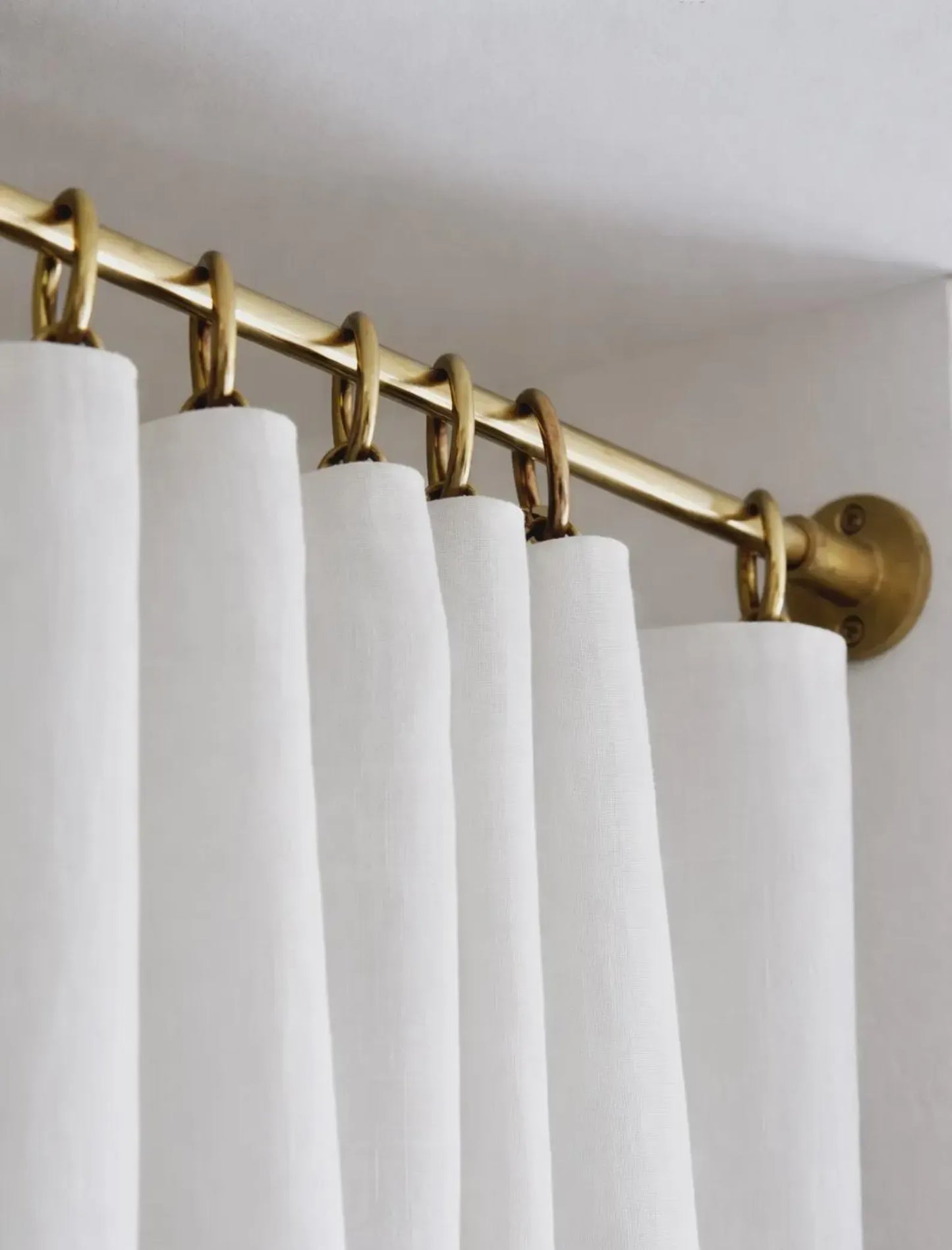 white curtains hanging on brass shower curtain rod